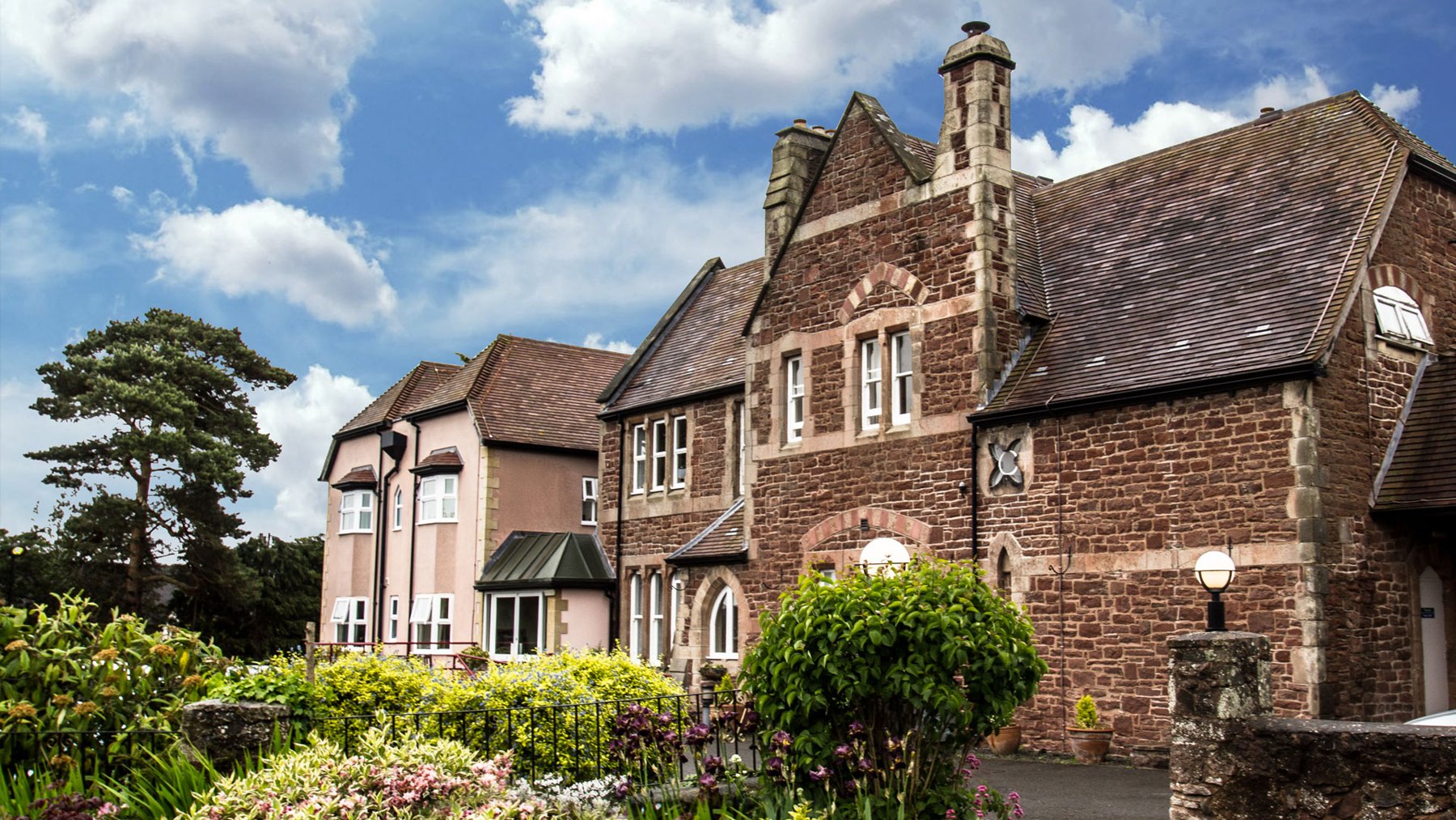 Stone and rendered frontage of an established care home behind planted gardens